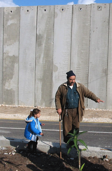 Hani and his daughter stand in the small area between their home and the Apartheid Wall built between them and their town, Mas&rsquo;ha.