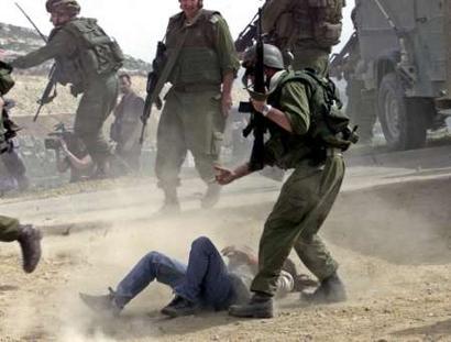 Female Israeli peace activist who was hurt after Israeli soldiers attacked the protestors, lies on the ground with an Israeli soldier standing over her.