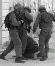 Three Israeli soldiers kick a Palestinian on his knees.